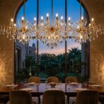 Grand modern crystal chandelierium with brushed brass arms suspended in a luxury high-ceiling room